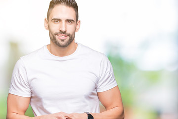 Handsome man wearing white t-shirt over outdoors background Hands together and fingers crossed smiling relaxed and cheerful. Success and optimistic