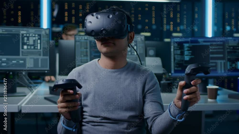 Fototapete Portrait of Software Delevoper Wearing Virtual Reality Headset Using Controllers to Develop and Program VR Gaming and Applications. In the Background Technology Developing Studio with Computers