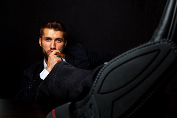 Portrait eines attraktiven bärtigen Geschäftsmannes mit Zigarre und die Beine auf dem Tisch....