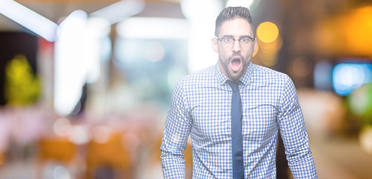 Young business man wearing glasses over isolated background In shock face, looking skeptical and sarcastic, surprised with open mouth