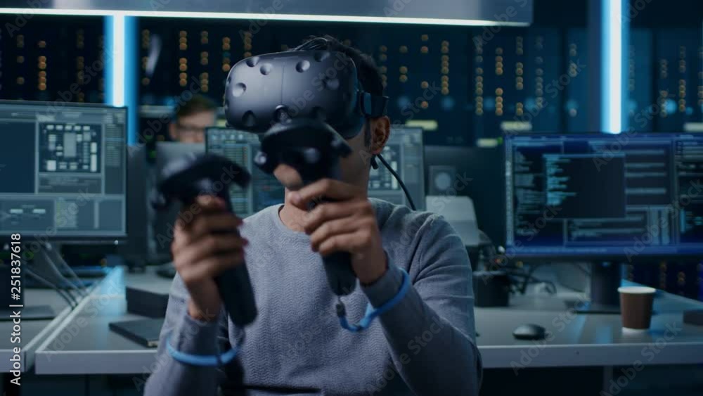 Aufkleber Portrait of Software Delevoper Wearing Virtual Reality Headset Using Controllers to Develop and Program VR Gaming and Applications. In the Background Technology Developing Studio with Computers
