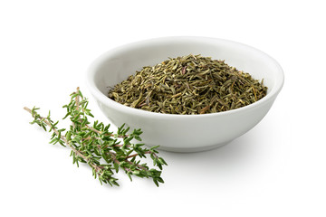 Dried rubbed thyme in a white ceramic bowl next to fresh thyme sprigs isolated on white.