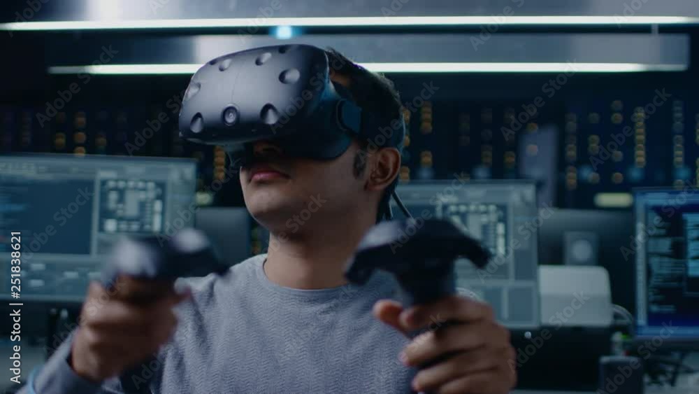 Aufkleber Software Delevoper Wearing Virtual Reality Headset Using Controllers to Develop and Program VR Gaming and Applications. In the Background Technology Developing Studio with Computers and Monitors