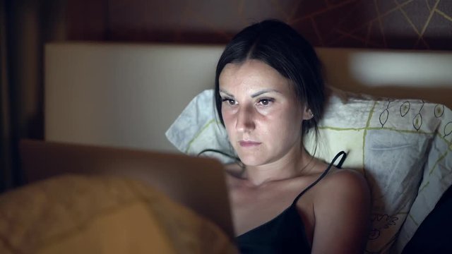 Woman lying on bed and working on laptor. girl working on a computer at night in bed