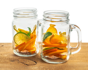 jars with lemon, orange, lime, twig mint without liquid on wooden background isolated, concept of refreshing summer drink