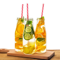 bottles of infused detox water with lemon, orange, lime, twig mint, cucumber, ginger and straws on wooden background isolated, concept of refreshing summer drink