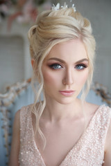 Gentle portrait of an elegant blonde bride in a light pink dress in the interior.