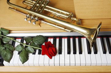 Trumpet and red rose on the piano keyboard.