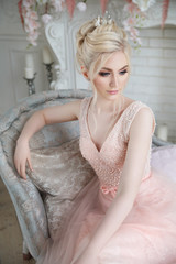 Gentle portrait of an elegant blonde bride in a light pink dress in the interior.