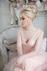 Gentle portrait of an elegant blonde bride in a light pink dress in the interior.