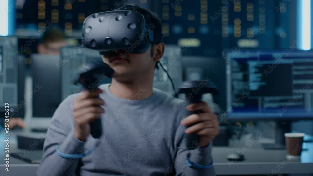 Aufkleber Software Delevoper Wearing Virtual Reality Headset Gesturing with Controllers to Develop and Program VR Gaming and Applications. In the Background Technology Developing Studio with Computers  Monitors
