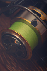 Fishing reel for a fishing rod with a green fishing line. Blurred toned photo. Hobby. Sport. Wooden background.