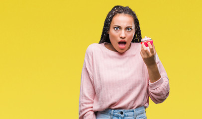 Young african american girl eating cupcake over isolated background scared in shock with a surprise...