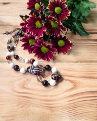 Murano glass beads and a bouquet of maroon chrysanthemums on a wooden table. Composition of handmade women's jewelry to the women's day.