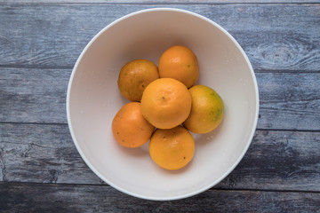 Fresh oranges in white bowl on wooden table background.
