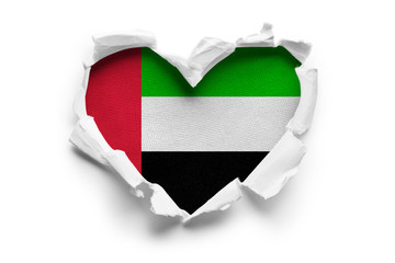 Heart shaped hole torn through paper, showing satin texture of flag of United Arab Emirates....