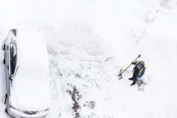Man shoveling snow near cars on road, parking