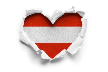 Heart shaped hole torn through paper, showing satin texture of flag of Austria. Isolated on white...