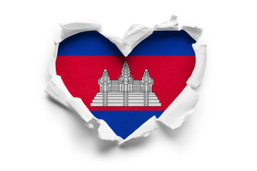 Heart shaped hole torn through paper, showing satin texture of flag of Cambodia. Isolated on white...