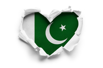 Heart shaped hole torn through paper, showing satin texture of flag of Pakistan. Isolated on white background