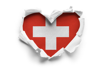 Heart shaped hole torn through paper, showing satin texture of flag of Switzerland. Isolated on...