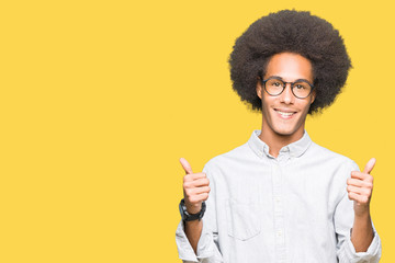 Young african american man with afro hair wearing glasses success sign doing positive gesture with hand, thumbs up smiling and happy. Looking at the camera with cheerful expression, winner gesture.