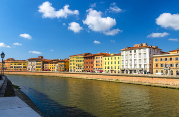 Fototapeta na wymiar Row of old colorful buildings houses on embankment promenade of Arno river in historical centre of Pisa town with blue sky white clouds copy space background in sunny day, Tuscany, Italy