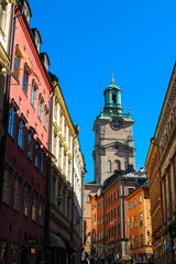 Fototapeta na wymiar View onto Sankt Nikolai kyrka in Stockholm through a typical Swedish alley with colourful houses and cloud-free blue sky (Stockholm, Sweden, Europe)