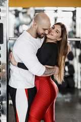 Obraz premium Romantic happy athletic couple. Strong man and slender beautiful girl are hugging in the modern gym next to the sport equipment