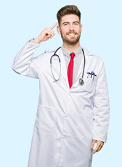 Young handsome doctor man wearing medical coat Smiling pointing to head with one finger, great idea or thought, good memory