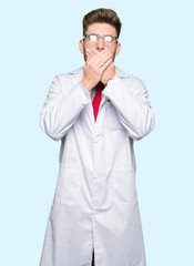 Young handsome scientist man wearing glasses shocked covering mouth with hands for mistake. Secret concept.