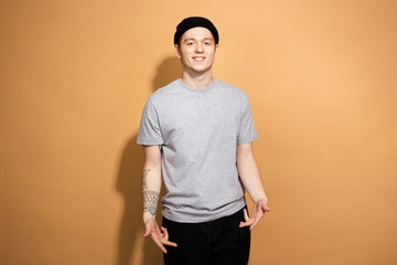 Smiling guy dressed in a gray shirt, black jeans and black hat with tattoo on his hand is posing on...