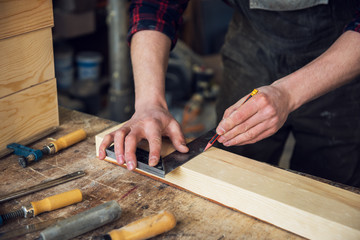The worker makes measurements of a wooden board with ruler.
