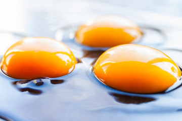 Three fresh raw chicken eggs spilled on a dark pan	