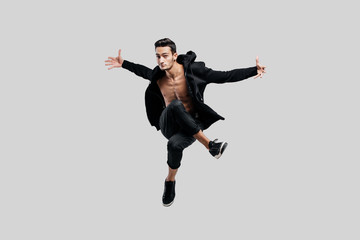 Handsome dancer of street dancing dressed in black pants and a sweatshirt on a naked torso jumps and spreads his arms to the sides