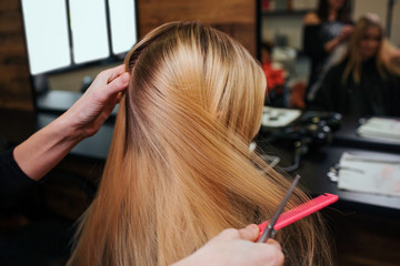 Naklejka premium Hairstylist hands combing blonde hair before hair care procedures in beauty salon