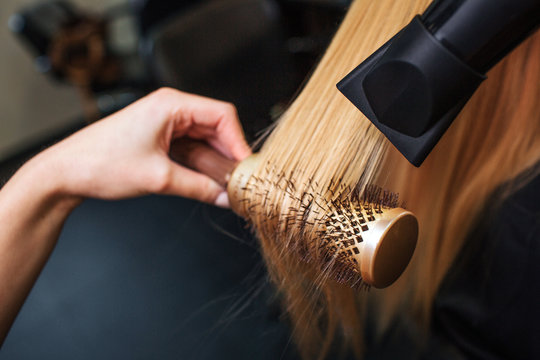 Close-up of hairdressers hand drying blond hair with hair dryer and round brush. Doing hairstyle in beauty salon