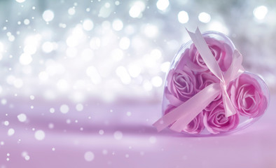 Box with pink roses inside in the form of a heart on a light background bokeh. Blurred white lights