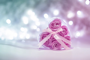 Box with pink roses inside in the form of a heart on a light background bokeh. Blurred white lights