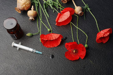  Red poppies and poppy heads and medical syringe on the table. Drugs.