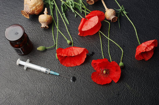  Red poppies and poppy heads and medical syringe on the table. Drugs.