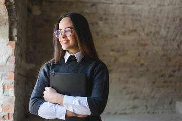 Brunette girl wearing glasses standing with exercise book at the loft placement and looking to the window