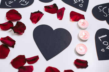 Black valentines and petals of red roses on a white background. Fire decorative candles