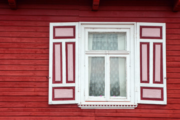 Red paint wooden rustic window in small cottage house. Vintage wall with transparent glass window and decorative red and white shutter.