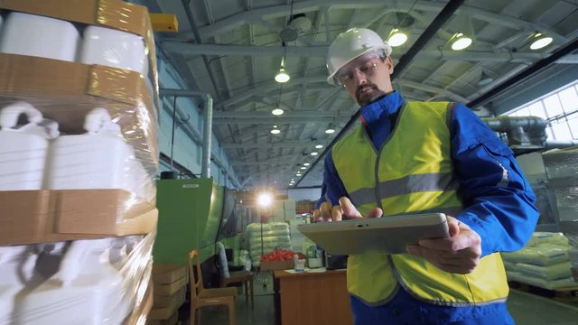 Man types on a tablet while watching a wrapping machine works.