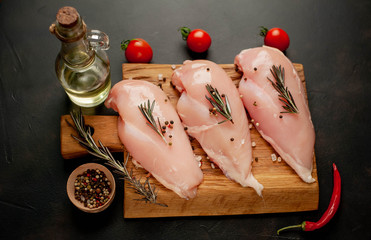 Raw chicken breast fillets, ready for cooking on a wooden cutting board with spices. on a specific background