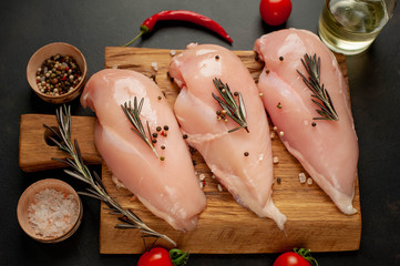 Raw chicken breast fillets, ready for cooking on a wooden cutting board with spices. on a specific...