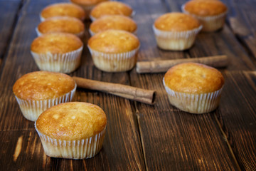 Fresh golden muffins and cinnamon sticks lie on a wooden surface made of pine boards. Tasty and healthy food