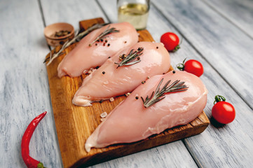 Raw chicken breast fillets ready for cooking on a wooden cutting board with spices. on a wooden...