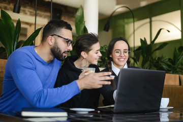 Group of friends chatting and using laptop in cafe in university talking and laughing together